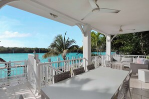 A covered outdoor seating area with a view of a turquoise sea and palm trees. - Luxury Waterfront 5BD/4Bth private pool 36' dock (Marathon)