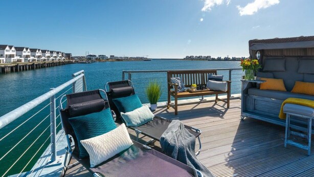 A deck with lounge chairs and a sofa overlooking a body of water with a pier in the background. - Houseboat in Kappeln With Swimming Pool (Kappeln)
