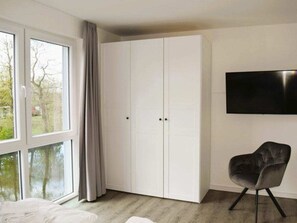 Ein Schlafzimmer mit großem Kleiderschrank, einem Bett, einem Sessel und einem Fernseher an der Wand.