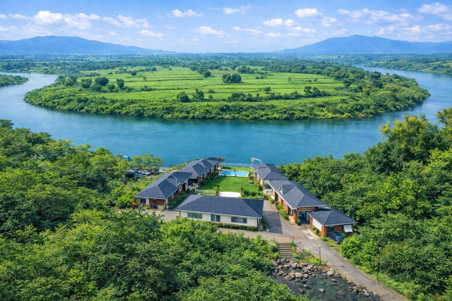 A riverside hotel with multiple buildings, a swimming pool, and lush greenery.