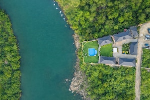 An aerial view of a property with a swimming pool, a tennis court, and a parking area.