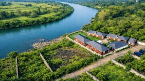 A riverside property with multiple brick houses, a well-maintained lawn, and a clear view of the river. - Necklace Bluewater Resort Bhor (Sangamner)