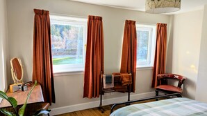 Une chambre à coucher avec un lit, une chaise, un bureau avec un miroir et une fenêtre avec des rideaux.
