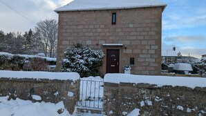 Un bâtiment en pierre, avec un toit enneigé et une entrée fermée par un portail.