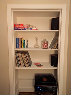 A bookshelf with various board games, books, a vinyl record player, and a decorative glass bottle.
