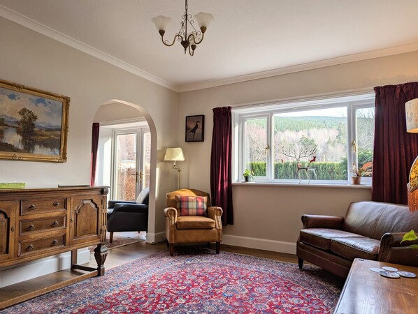 A room with a large window, a chandelier, a wooden cabinet, a sofa, and a patterned rug.
