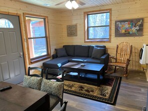 Interior acolhedor de uma cabana com sofá seccional, mesa de jantar e uma poltrona de balanço.