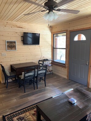 A wooden interior with a dining table, chairs, a television mounted on the wall, and a door with a window.