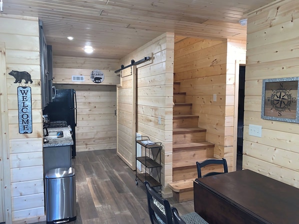 A wooden cabin interior with a kitchen, a dining area, and a staircase.