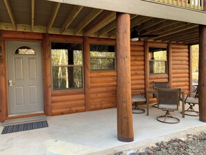 A log cabin with a covered porch, a dining area with metal chairs, and a door with a window.