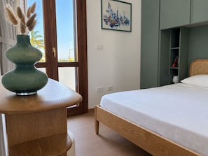 A bedroom with a bed, a wooden nightstand, a green vase with pampas grass, a painting on the wall, and a view through an open door. - Boutique Apartment near the Sea with Rooftop Terrace – Santa Maria al Bagno (Nardò)
