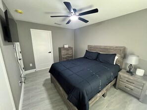 Ein Schlafzimmer mit Bett, Nachttischen, Kommode, Deckenventilator und einer Tür.