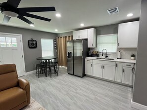 Eine moderne Küche mit weißen Schränken, einem Edelstahlkühlschrank, einem Esstisch mit Stühlen und einem Deckenventilator.