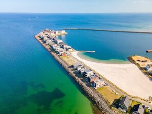 An aerial view of a coastal area with a long pier, a sandy beach, and a row of buildings along the water's edge. - NEW - Sky 65 Plus (Kappeln)