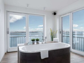 A modern bathroom with a large bathtub, a view of the water, and a balcony with a railing. - NEW - Sky 65 Plus (Kappeln)