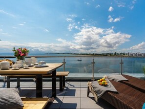 A dining area with a table set for two, overlooking a body of water with a view of buildings in the distance. - NEW - Sky 65 Plus (Kappeln)