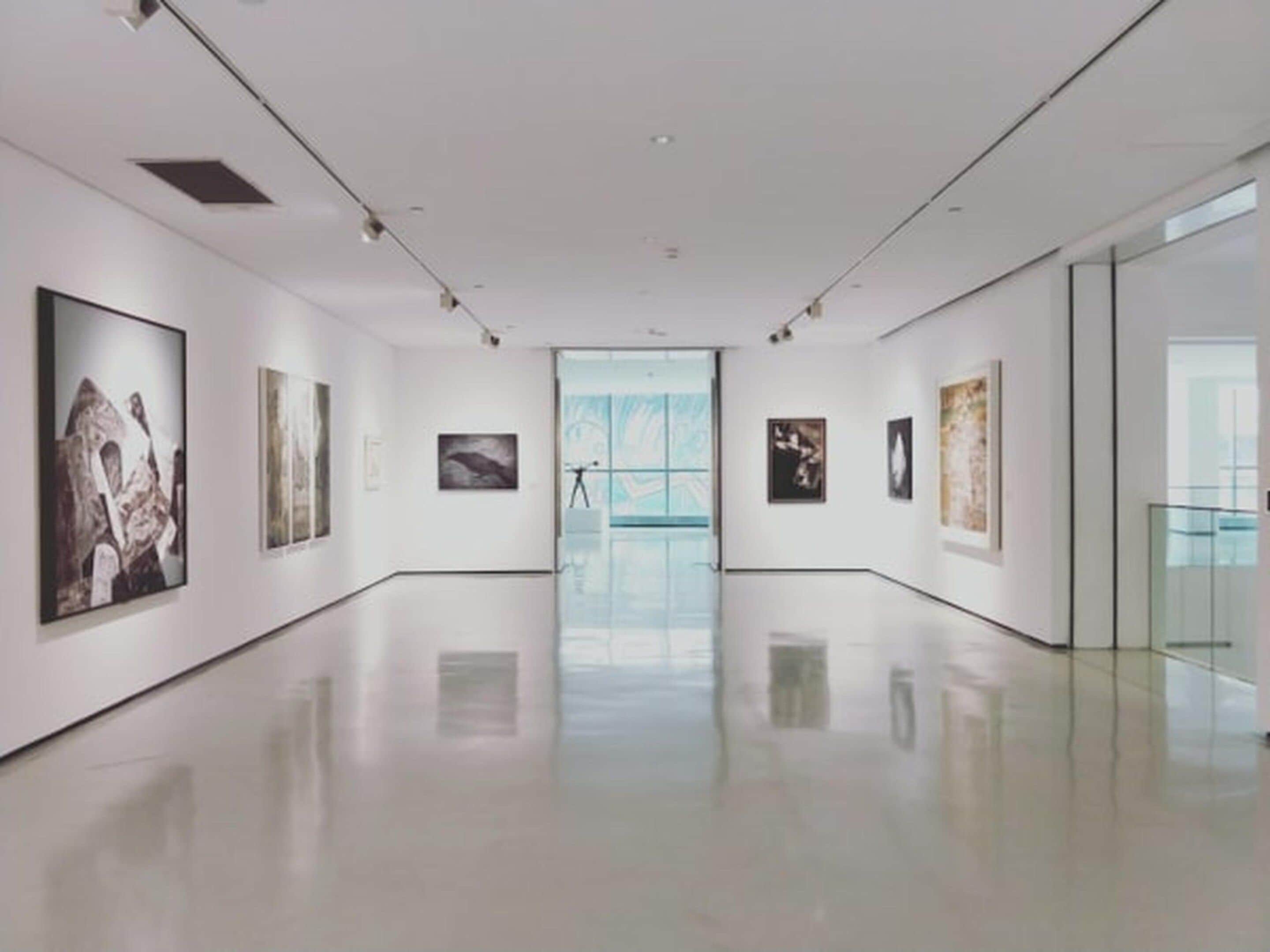 A spacious gallery with a polished floor, white walls, and artwork displayed on both sides.