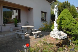 A patio area with a stone table and benches, a statue, and a well-maintained garden. - Holiday Residence in North Vosges (Bitche)