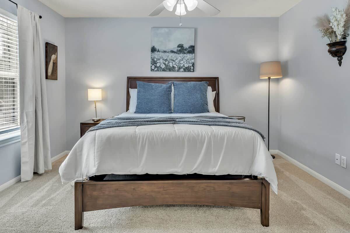 Une chambre à coucher avec un lit, une lampe de chevet, un tableau au mur et une fenêtre avec des rideaux.