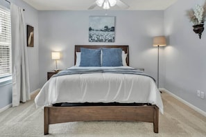 Une chambre à coucher avec un lit, une lampe de chevet, un tableau au mur et une fenêtre avec des rideaux.