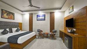 A hotel room with a bed, a desk, a TV, and a small table with chairs. - Hotel Rise Free Airport Pickup  (New Delhi)