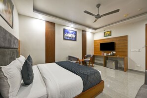 A modern hotel room with a large bed, a desk, a chair, a television, and a ceiling fan. - Hotel Rise Free Airport Pickup  (New Delhi)