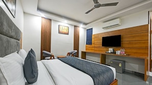 A hotel room with a bed, two chairs, a desk, a television, and an air conditioning unit. - Hotel Rise Free Airport Pickup  (New Delhi)