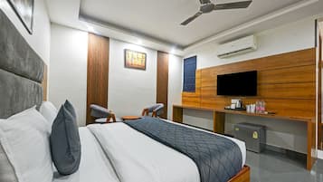 Quarto de hotel com cama, duas cadeiras, escrivaninha, televisão e aparelho de ar condicionado.