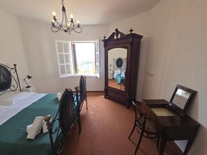 Ein Schlafzimmer mit einem Bett, einem Sessel, einem Schreibtisch, einem Spiegel und einer Kandelaber.
