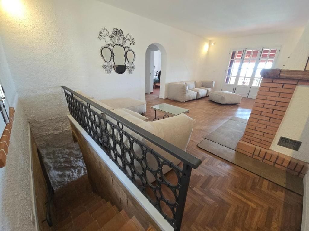 Ampla sala de estar com escada, lareira e vista através de um arco.