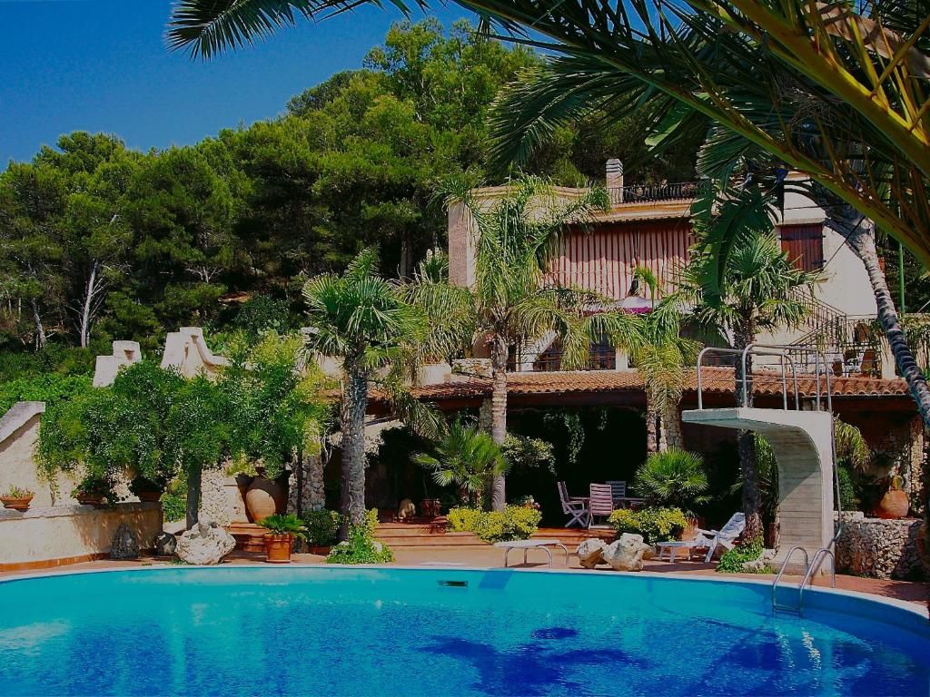Un área de piscina con una piscina azul cristalina, rodeada de palmeras y plantas en macetas.