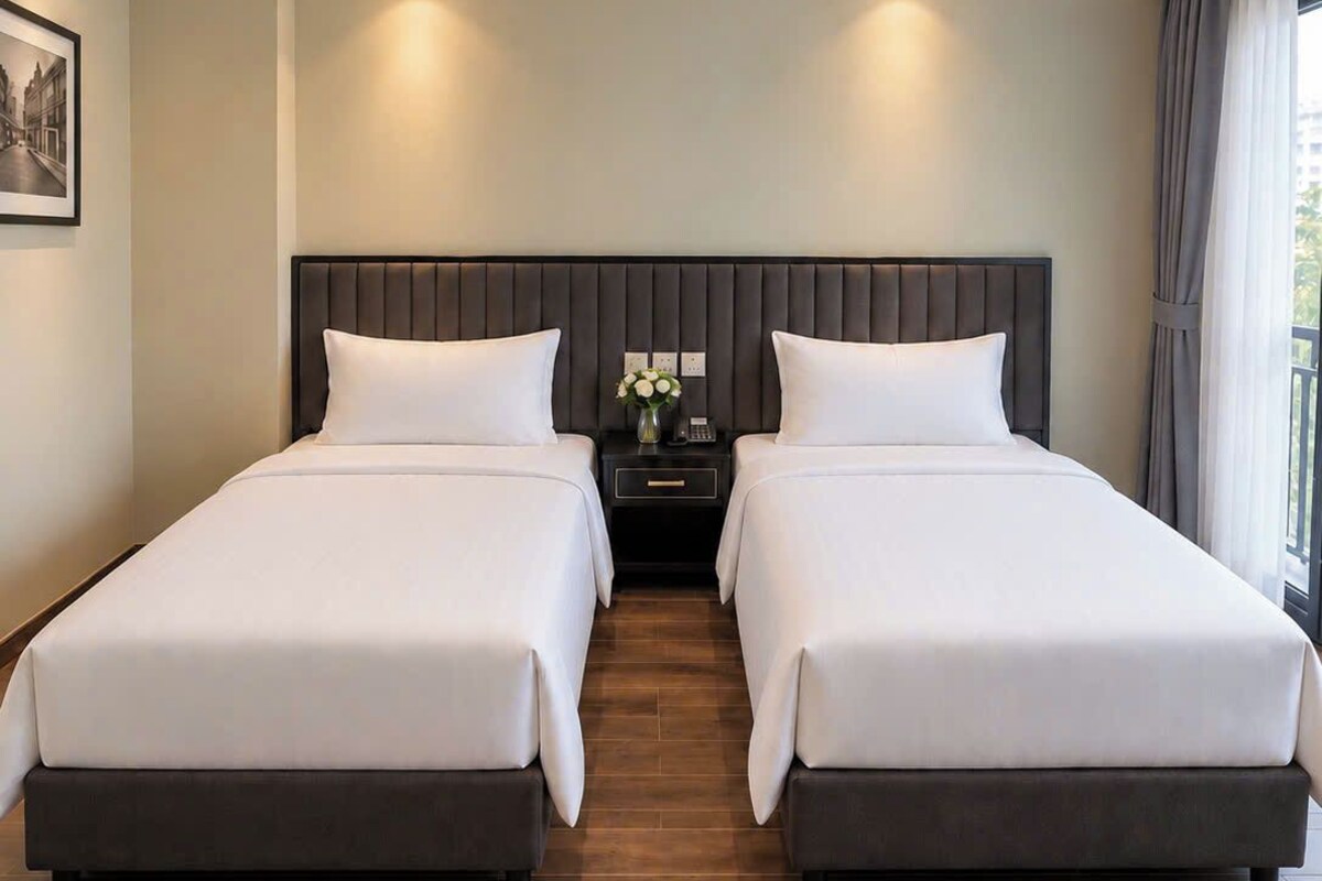 Habitación de hotel con dos camas, una mesita de noche con teléfono, un jarrón con flores y un cuadro en la pared.