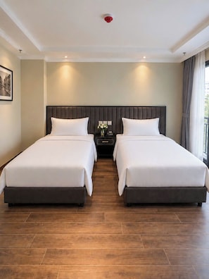 Habitación de hotel con dos camas, una mesita de noche con teléfono, un jarrón con flores y un cuadro en la pared.