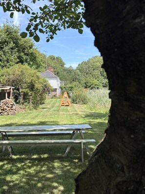 A picnic table in a grassy area with a house and trees in the background. - Beautiful coastal cottage in stunning National Trust Parkland with nearby beach! (Winchelsea)