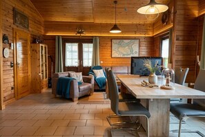 Interior de una cabaña de madera con comedor, asientos y un mapa en la pared.