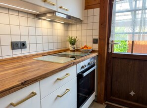 Una cocina con armarios blancos, encimera de madera, estufa y ventana con vistas a la vegetación.