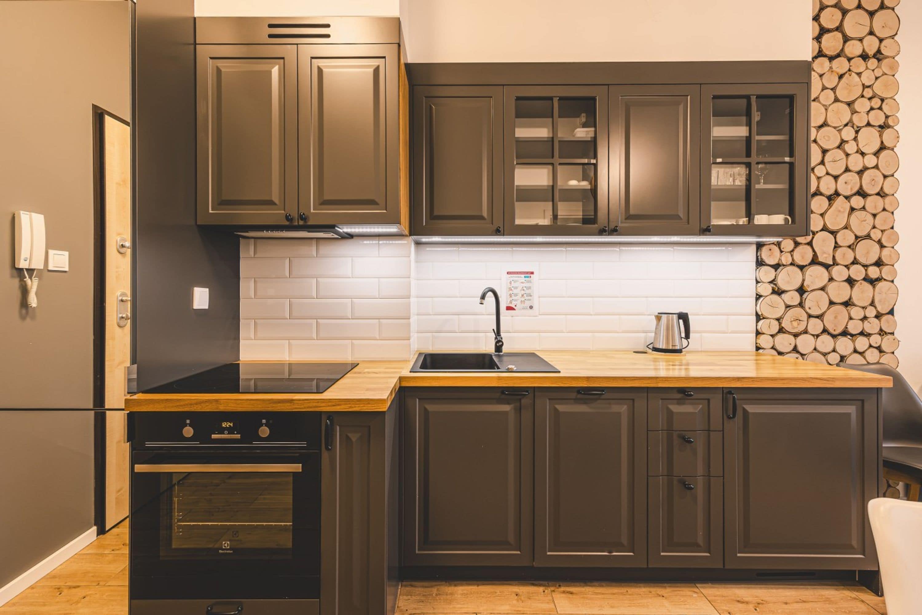 A modern kitchen with dark cabinetry, a wooden countertop, a stainless steel sink, and a built-in oven.