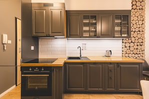 A modern kitchen with dark cabinetry, a wooden countertop, a stainless steel sink, and a built-in oven.