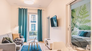 Una sala moderna con un sofá, una mesa de comedor para dos personas y un televisor montado en la pared.