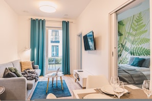 Un salon moderne avec un canapé, une table à manger pour deux personnes et un téléviseur fixé au mur.