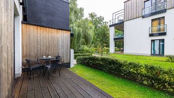A modern outdoor patio with a wooden deck, a table with chairs, and a well-maintained garden.