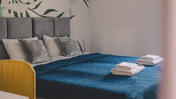 A hotel room with a bed, pillows, a blue quilted bedspread, and a chair.