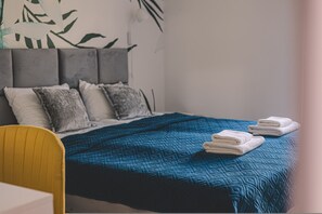 A hotel room with a bed, pillows, a blue quilted bedspread, and a chair.