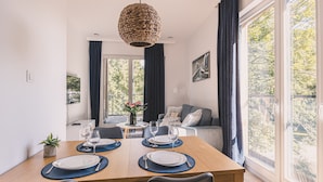 Un comedor con una mesa de madera dispuesta para cuatro personas, una lámpara colgante de fibras naturales y vistas al exterior a través de amplios ventanales.