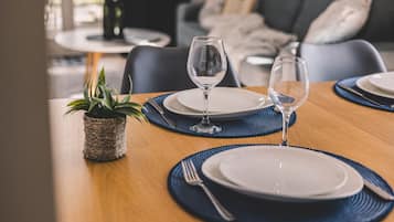 A dining table set with plates, cutlery, and glasses, with a plant on the side.