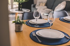 A dining table set with plates, cutlery, and glasses, with a plant on the side.