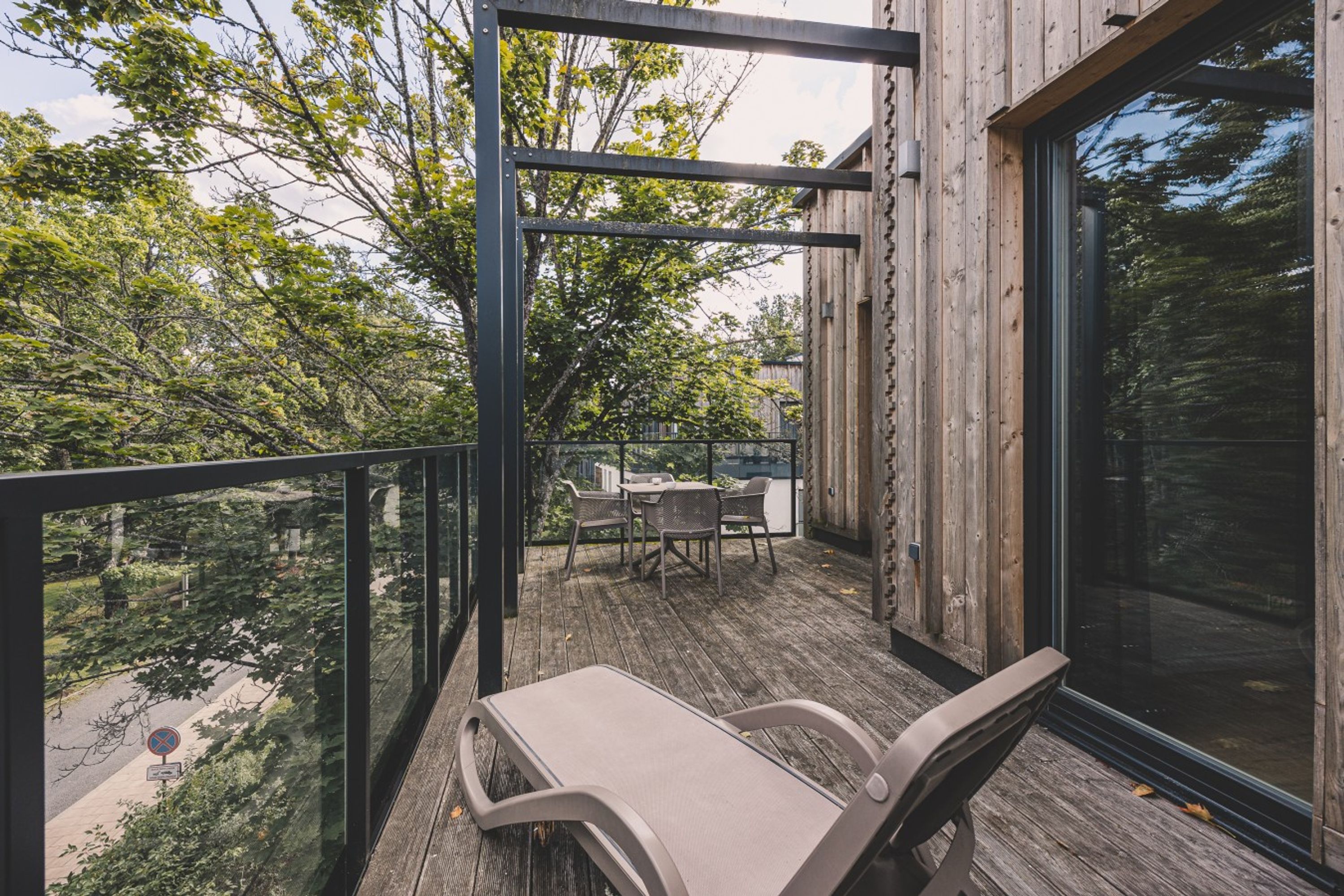A wooden deck with a glass balustrade, outdoor furniture, and a view of trees.