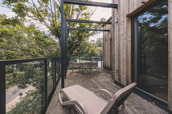 A wooden deck with a glass balustrade, outdoor furniture, and a view of trees.