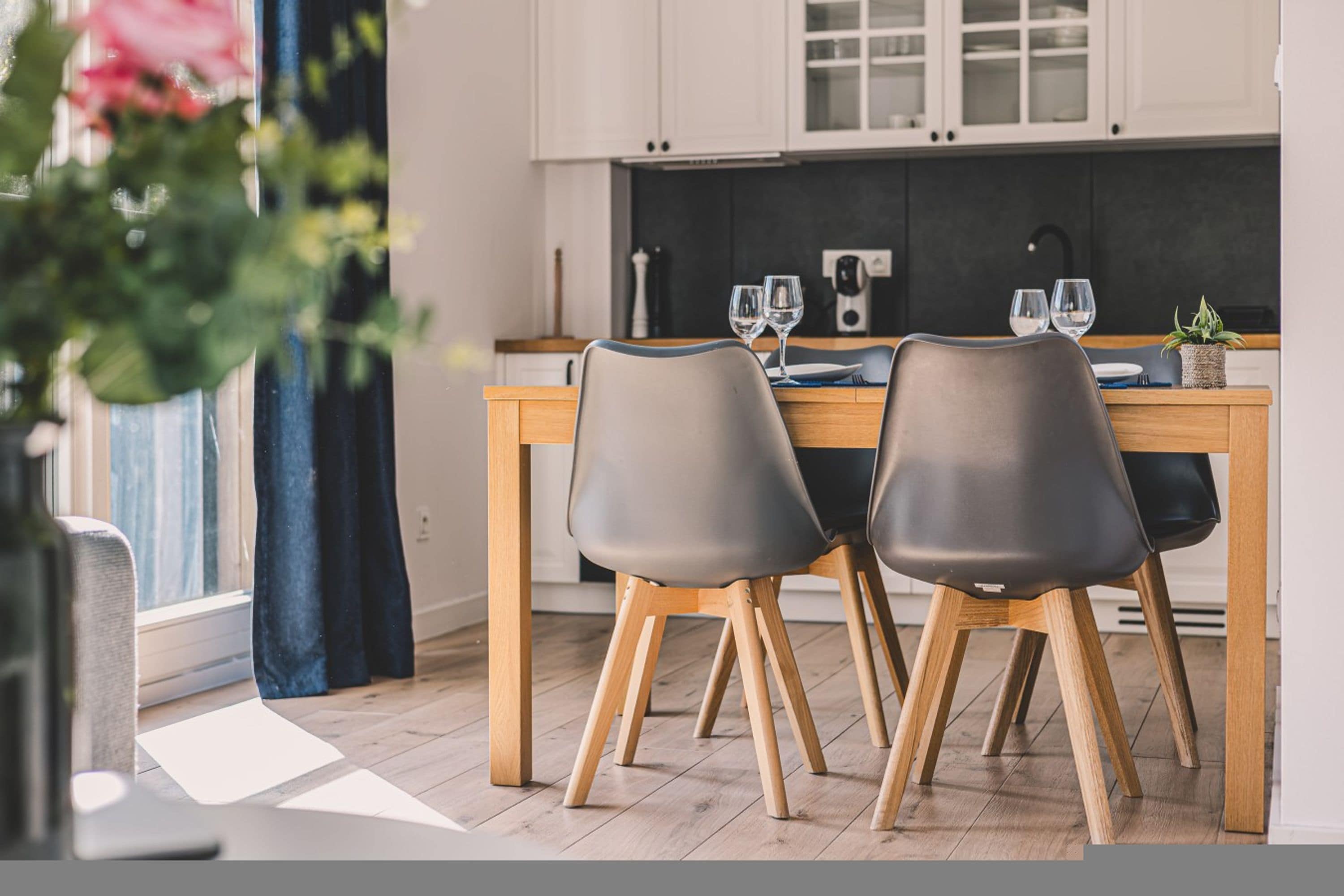 A modern kitchen with wooden cabinets, a dining table with two chairs, and a potted plant on the table.