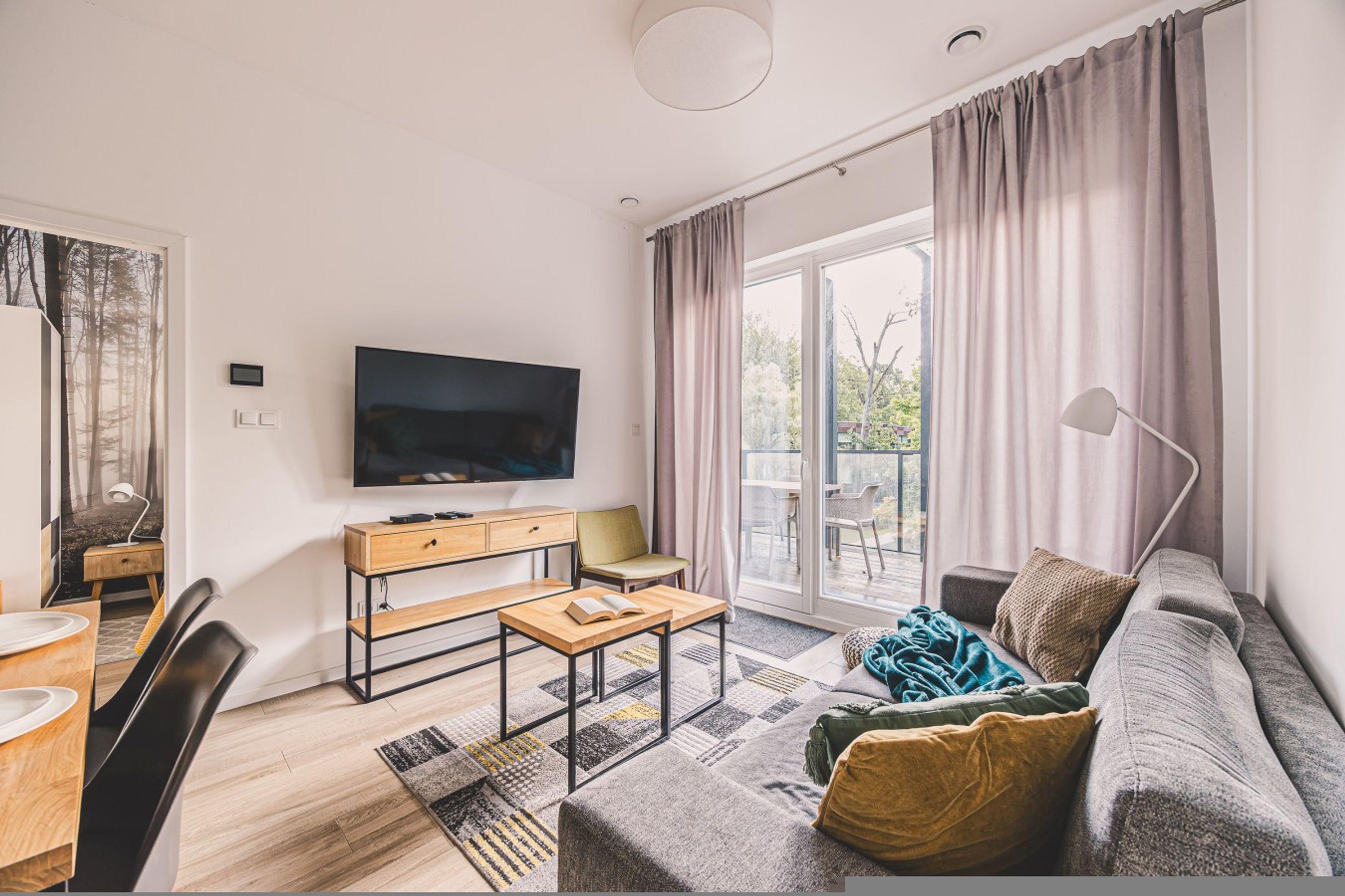Una sala de estar moderna con un televisor de pantalla plana, un sofá, una mesa de comedor y un ventanal corredero que da a un balcón.